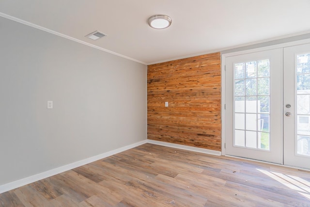 spare room featuring wooden walls, french doors, ornamental molding, and light hardwood / wood-style flooring