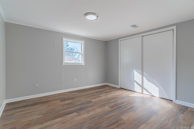 unfurnished bedroom with dark wood-type flooring, a closet, and ornamental molding