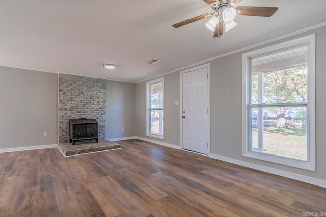 unfurnished living room featuring dark hardwood / wood-style flooring, ornamental molding, a wood stove, and a healthy amount of sunlight