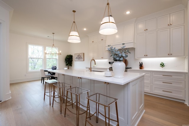 kitchen with white cabinets, hanging light fixtures, sink, light wood-type flooring, and a large island with sink