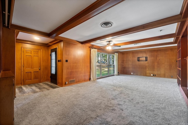 unfurnished living room featuring wood walls, beamed ceiling, ceiling fan, and light carpet