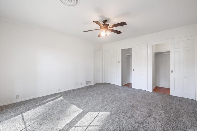 unfurnished bedroom with two closets, dark colored carpet, and ceiling fan