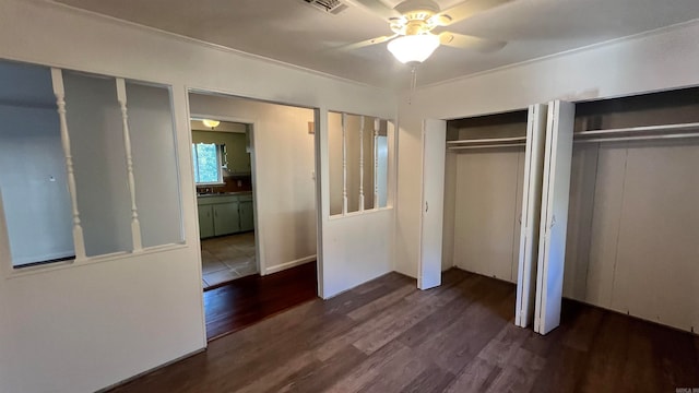 unfurnished bedroom with sink, dark hardwood / wood-style floors, ceiling fan, ornamental molding, and multiple closets