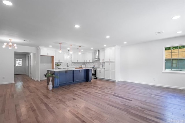 kitchen featuring stainless steel range with electric cooktop, a kitchen island, white cabinetry, wall chimney range hood, and light hardwood / wood-style floors