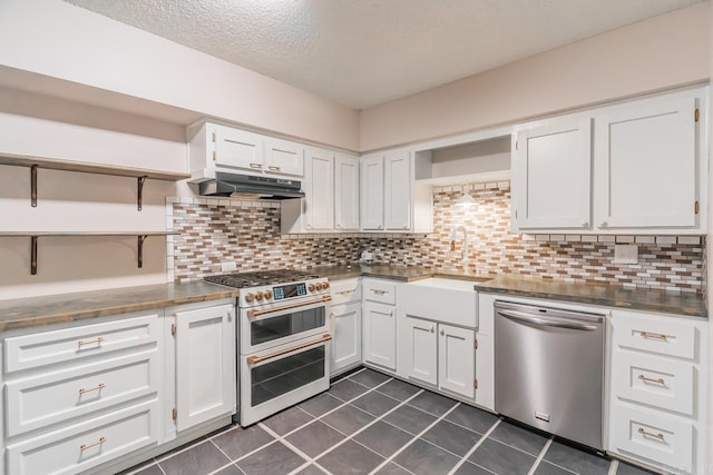 kitchen featuring stainless steel appliances, backsplash, dark tile patterned flooring, sink, and white cabinets