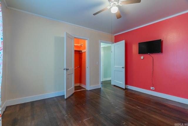 unfurnished bedroom featuring a closet, a spacious closet, crown molding, dark hardwood / wood-style floors, and ceiling fan