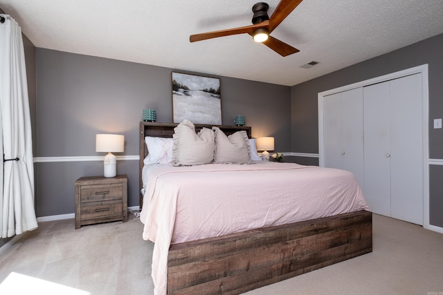 bedroom with a textured ceiling, light colored carpet, ceiling fan, and a closet