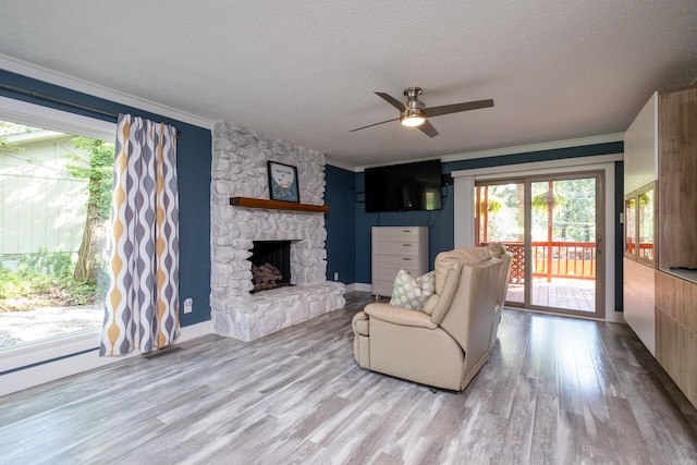 living room featuring ceiling fan, a textured ceiling, a fireplace, crown molding, and light wood-type flooring