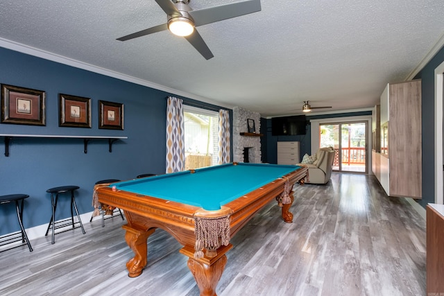 playroom featuring a stone fireplace, a textured ceiling, billiards, ceiling fan, and light hardwood / wood-style flooring