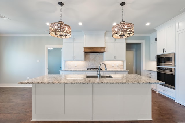 kitchen with light stone counters, appliances with stainless steel finishes, an island with sink, and white cabinets