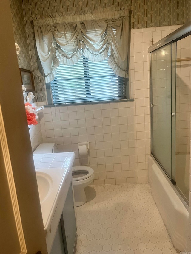 full bathroom with tile patterned floors, combined bath / shower with glass door, toilet, vanity, and tile walls