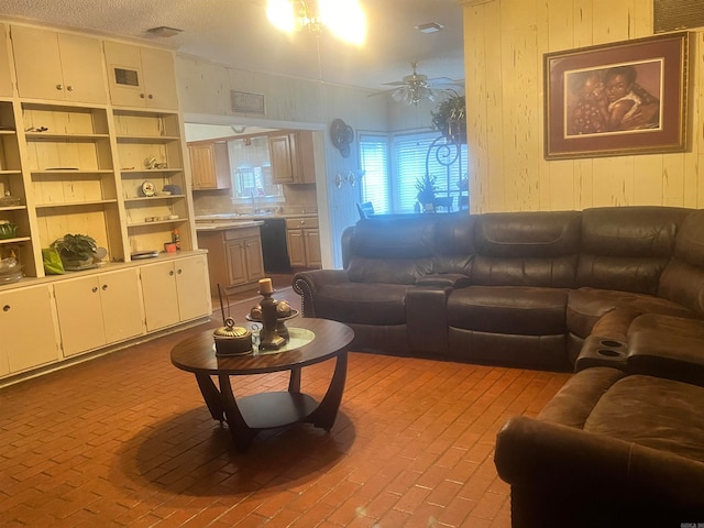 living room featuring wooden walls, ceiling fan, sink, and a textured ceiling