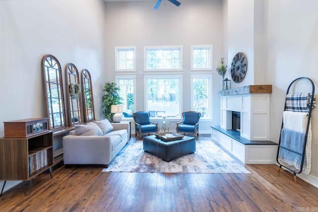 living room featuring a high ceiling, dark hardwood / wood-style flooring, ceiling fan, and a tiled fireplace