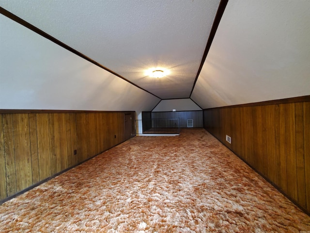 additional living space featuring carpet flooring, wooden walls, a textured ceiling, and lofted ceiling