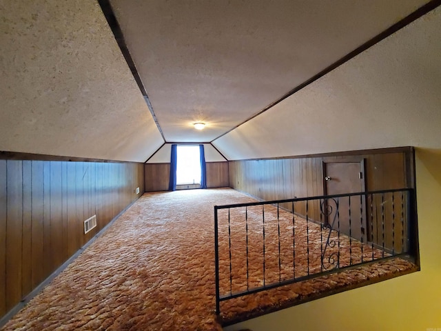 additional living space featuring a textured ceiling, carpet floors, vaulted ceiling, and wooden walls