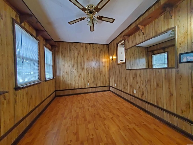 empty room featuring hardwood / wood-style floors, wood walls, ceiling fan, and plenty of natural light