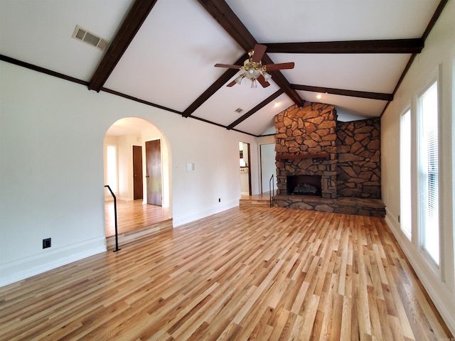 unfurnished living room featuring a stone fireplace, ceiling fan, light hardwood / wood-style flooring, and beamed ceiling