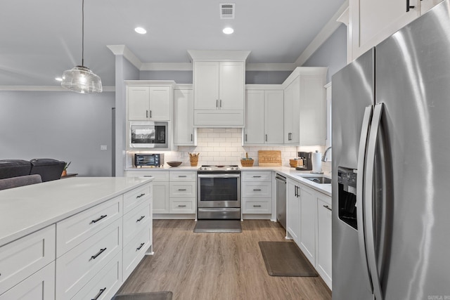 kitchen with ornamental molding, white cabinets, pendant lighting, decorative backsplash, and appliances with stainless steel finishes