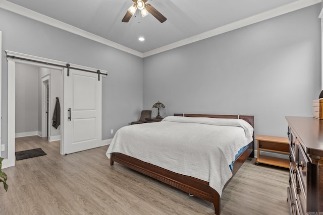 bedroom with ceiling fan, crown molding, a barn door, and light hardwood / wood-style floors