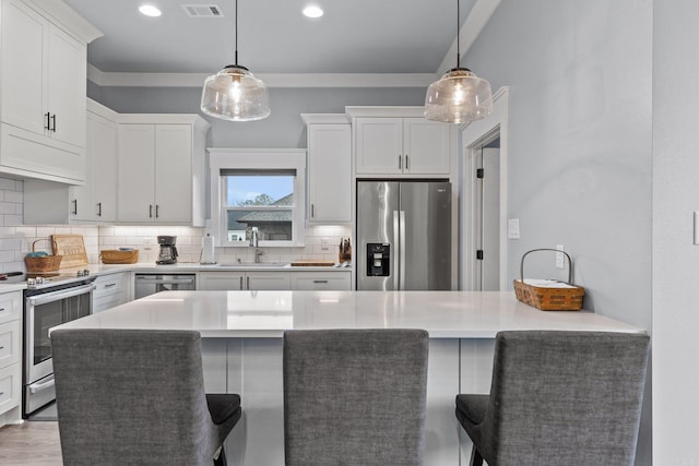 kitchen featuring a breakfast bar area, hanging light fixtures, white cabinets, and stainless steel appliances