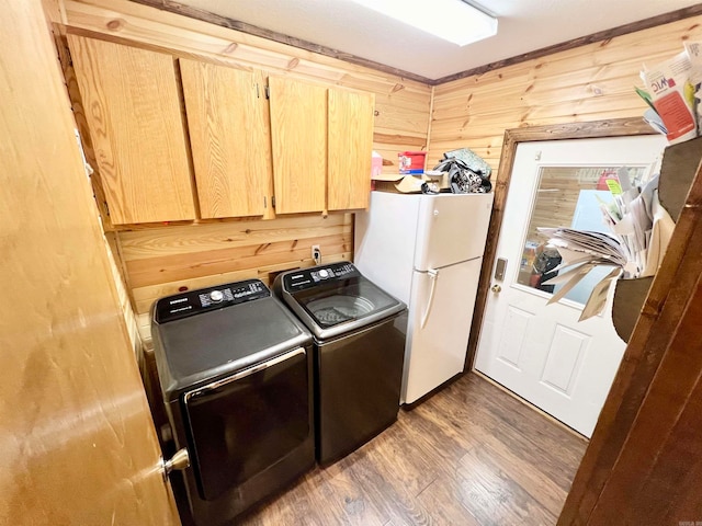 clothes washing area with wooden walls, dark wood-type flooring, cabinets, and washer and dryer