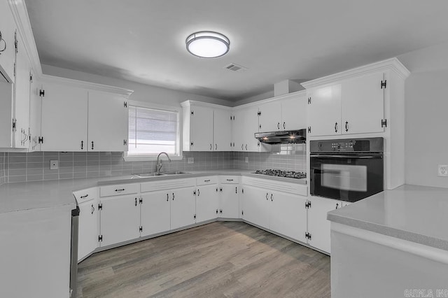 kitchen with black oven, white cabinetry, sink, and light hardwood / wood-style flooring