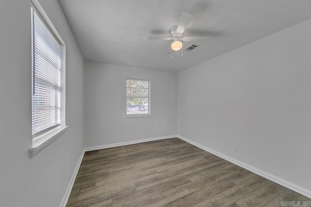 empty room featuring a wealth of natural light, ceiling fan, and dark wood-type flooring