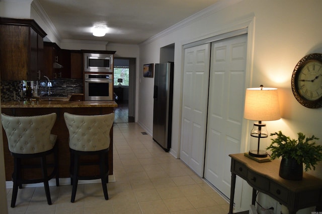 kitchen with backsplash, ornamental molding, dark brown cabinets, kitchen peninsula, and stainless steel appliances