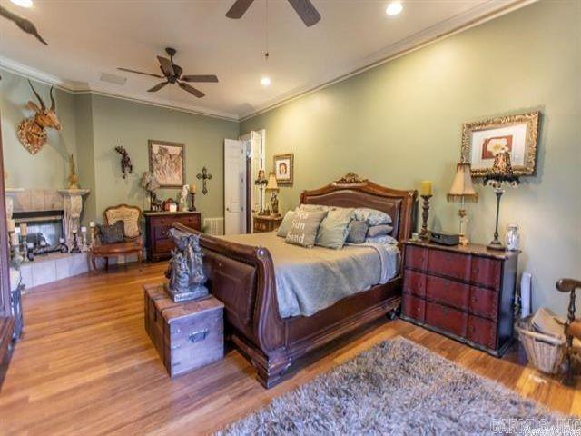 bedroom with ceiling fan, a multi sided fireplace, hardwood / wood-style floors, and crown molding