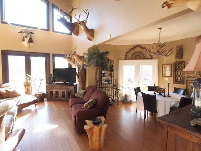 living room featuring french doors, wood-type flooring, ornamental molding, and a notable chandelier