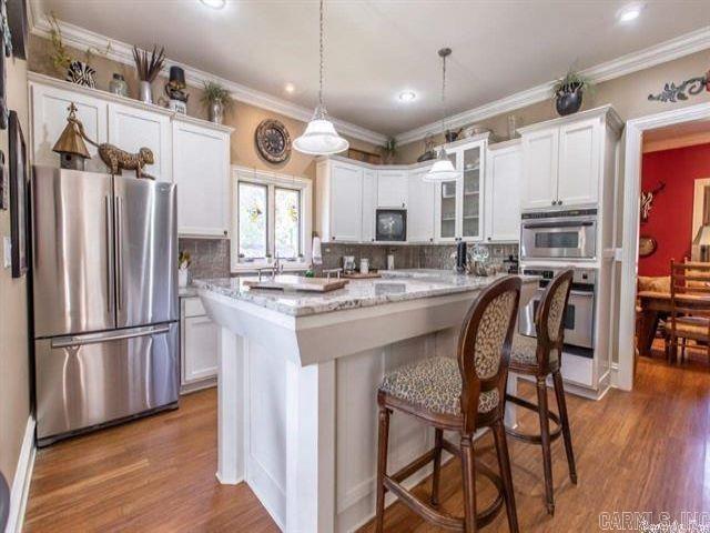 kitchen with white cabinets, stainless steel refrigerator, a kitchen island, and pendant lighting