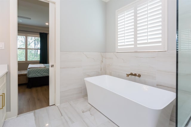 bathroom with a tub to relax in, hardwood / wood-style floors, vanity, and tile walls