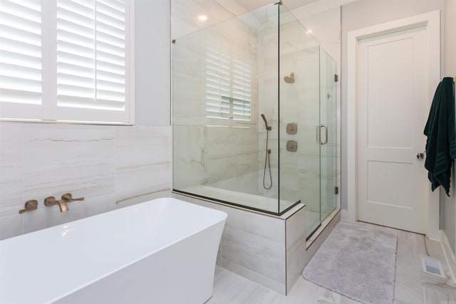 bathroom with shower with separate bathtub and tile walls