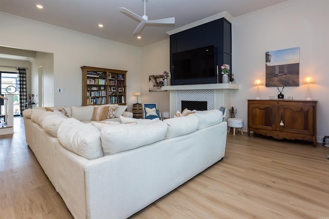 living room with a tiled fireplace, ceiling fan, crown molding, and light wood-type flooring