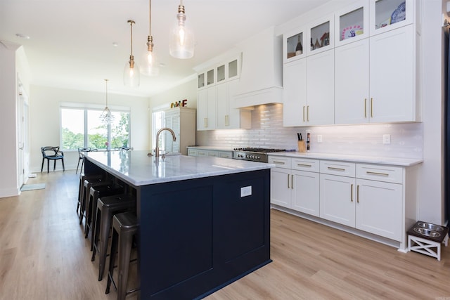 kitchen featuring white cabinets, pendant lighting, light wood-type flooring, and a kitchen island with sink