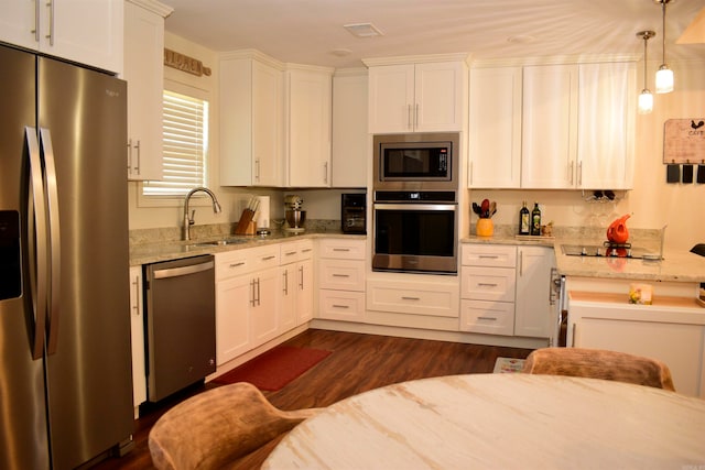 kitchen featuring appliances with stainless steel finishes, dark wood-type flooring, sink, pendant lighting, and white cabinetry