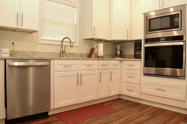 kitchen with light stone counters, white cabinets, dark wood-type flooring, and appliances with stainless steel finishes