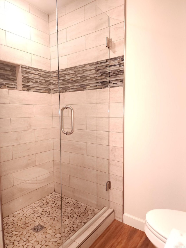 bathroom featuring a shower with shower door, toilet, and wood-type flooring