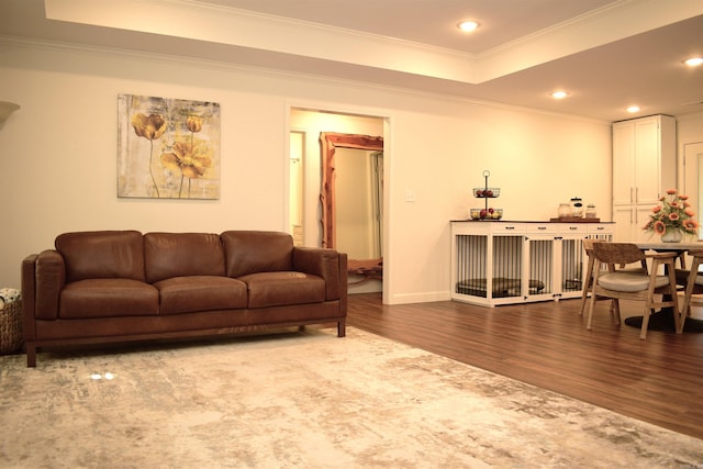 living room with hardwood / wood-style flooring, a raised ceiling, and ornamental molding