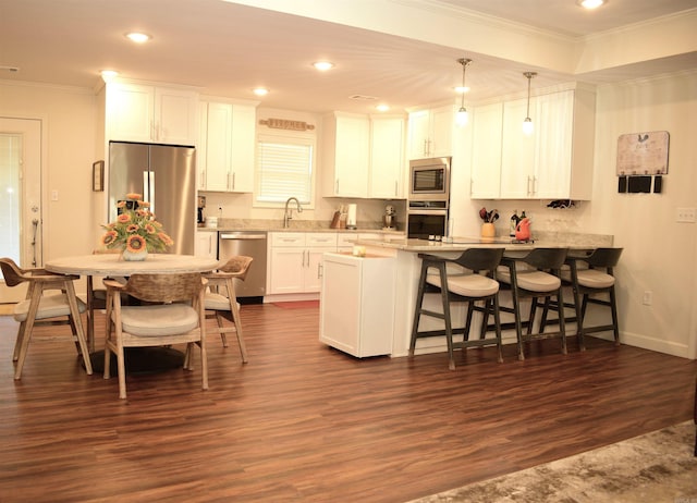 kitchen featuring appliances with stainless steel finishes, dark hardwood / wood-style flooring, ornamental molding, pendant lighting, and white cabinets