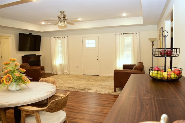 living room with a tray ceiling, crown molding, ceiling fan, and wood-type flooring