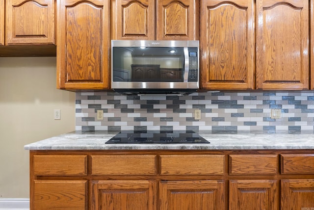 kitchen with black electric stovetop, light stone countertops, and tasteful backsplash