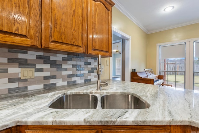 kitchen with decorative backsplash, crown molding, light stone countertops, and sink