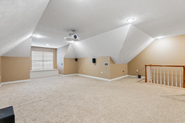 additional living space with vaulted ceiling, light colored carpet, and a textured ceiling