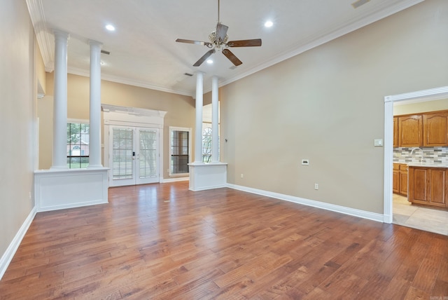 unfurnished living room featuring french doors, decorative columns, ornamental molding, ceiling fan, and light hardwood / wood-style flooring