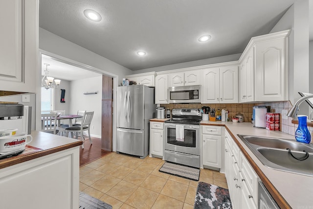 kitchen with stainless steel appliances, sink, light tile patterned floors, an inviting chandelier, and white cabinets