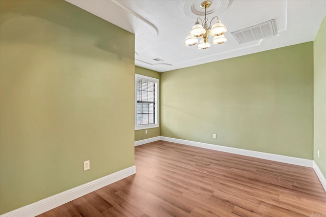 spare room with a chandelier and wood-type flooring