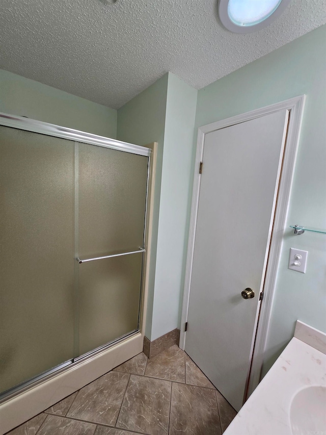 bathroom with tile patterned floors, a shower with door, vanity, and a textured ceiling