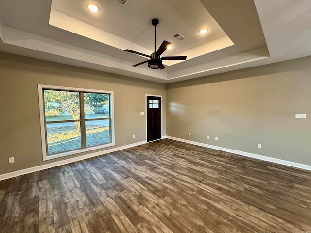 unfurnished room with a raised ceiling, ceiling fan, and dark hardwood / wood-style flooring