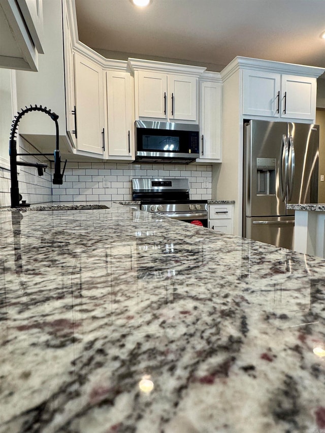 kitchen featuring decorative backsplash, stainless steel appliances, white cabinets, and light stone counters